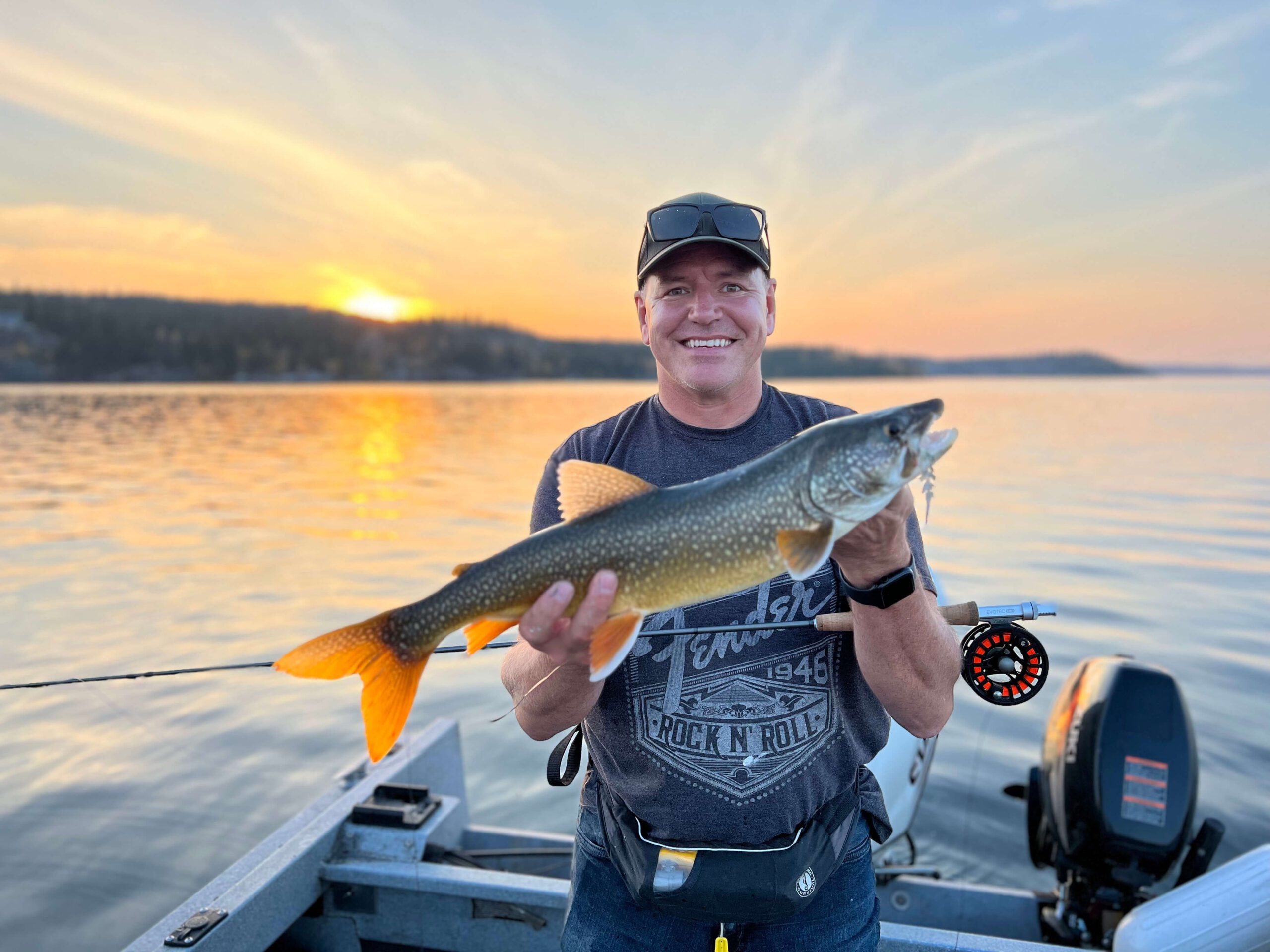 Man on a fly fishing excursion smiling and holding a fish he caught